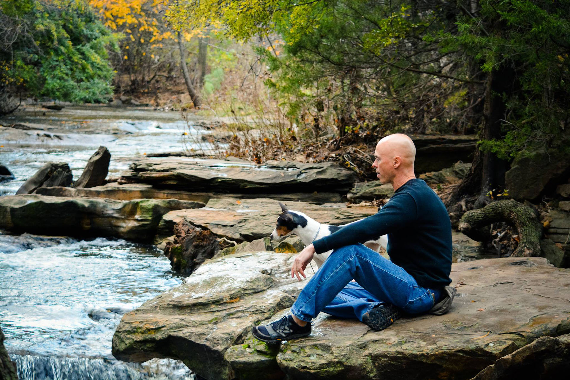 Tod McVicker sitting on the rocks by a creek with his dog
